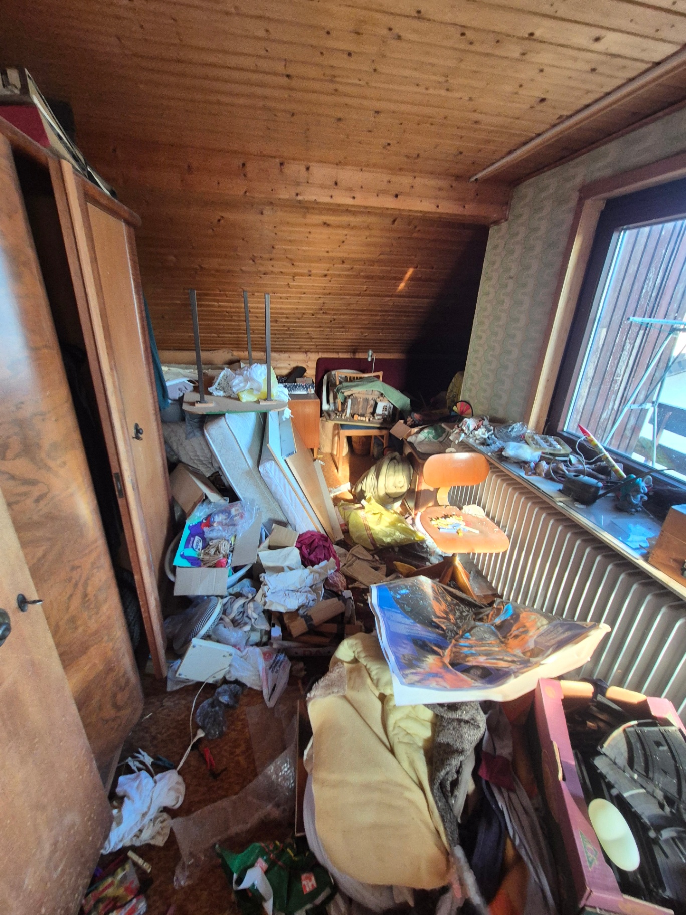 Überstelltes Dachzimmer mit Schränken, Stuhl, Kartons und losem Hausrat